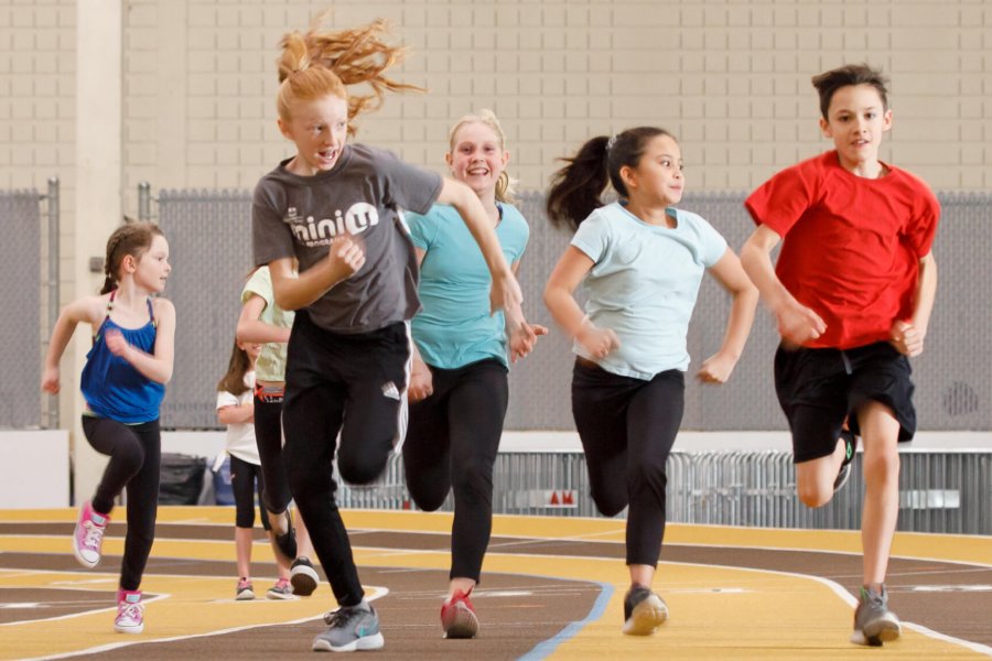 Several children racing each other on an indoor running track.