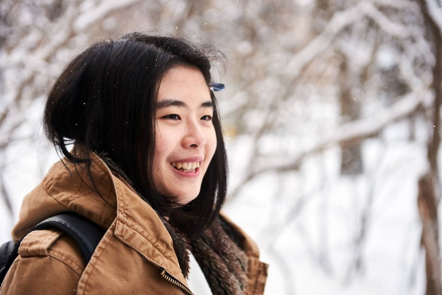 An international student stands smiling outdoors on a snowy winter day.