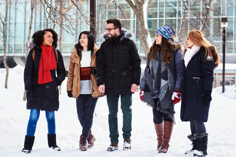 A group of 5 international students walk outdoors in the snow engaging in friendly conversation.