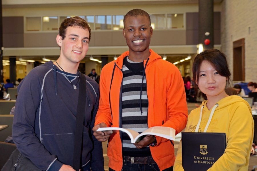 Three international students stand together in a library.