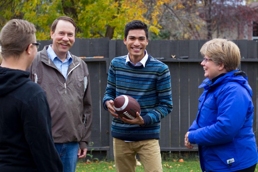 An international student stands in a backyard holding a football with his homestay family.