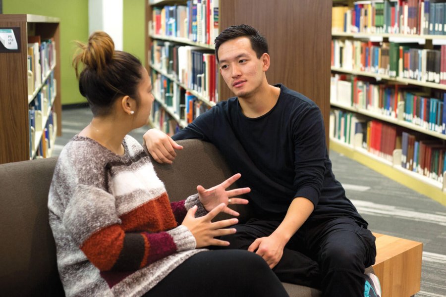 Two students sitting in a library together talking.