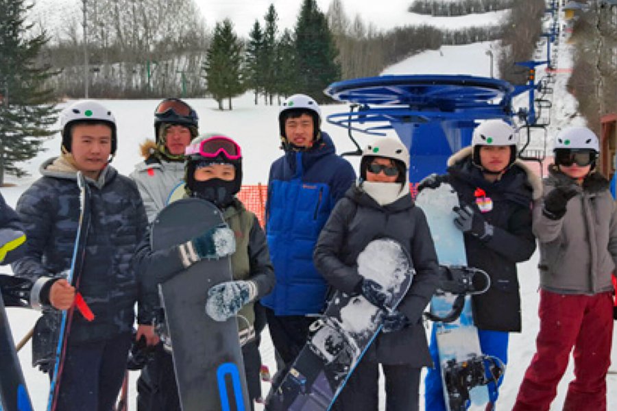 7 students stand together at a ski hill holding snowboards.