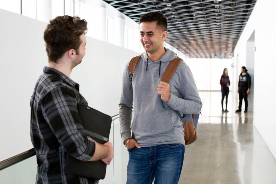 Two students stand in a hallway talking.