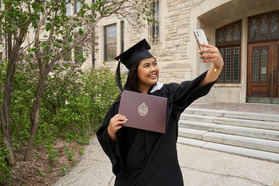 A student in her cap and gown taking a selfie showing her degree.