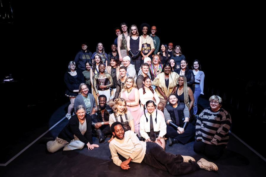 A large group photo of the cast and crew of The Comedy of Errors, on stage, with a spotlight shining on them.