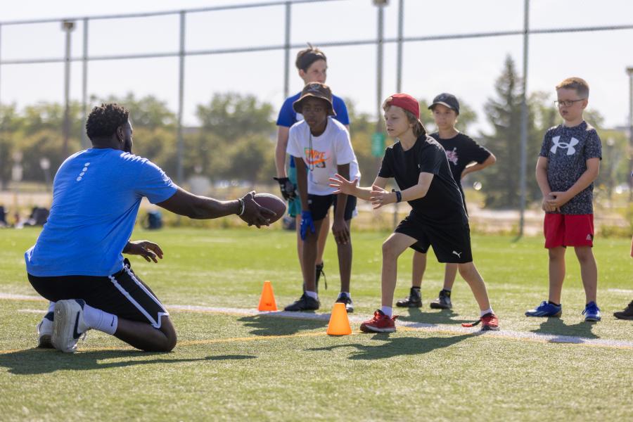 Summer camp staff passing football to a child