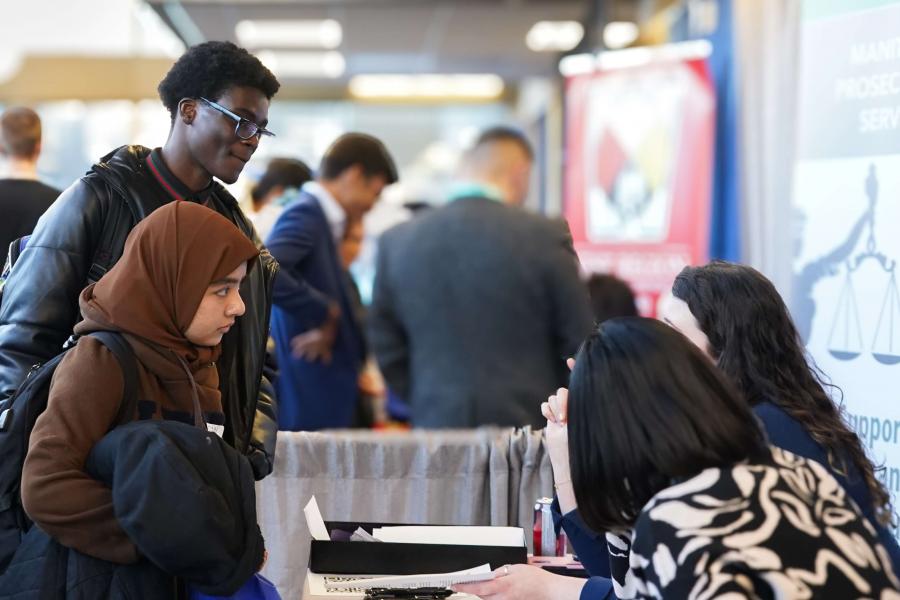 Two students listen two potential recruiters at a table at the Career Fair.