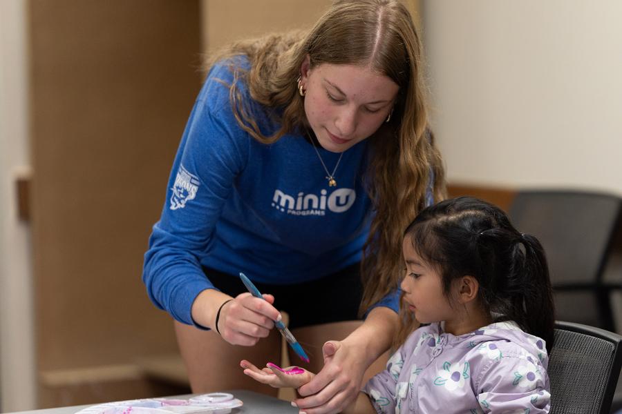 A young woman camp leader helps a young girl with finger paint.