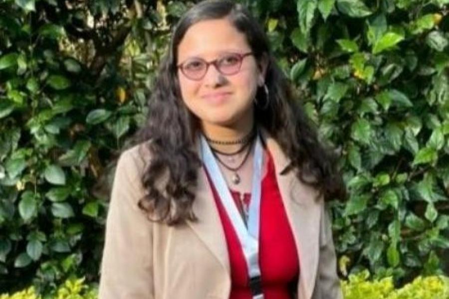 PIA, Yashi, standing in a red dress and beige blazer, smiling at the camera.