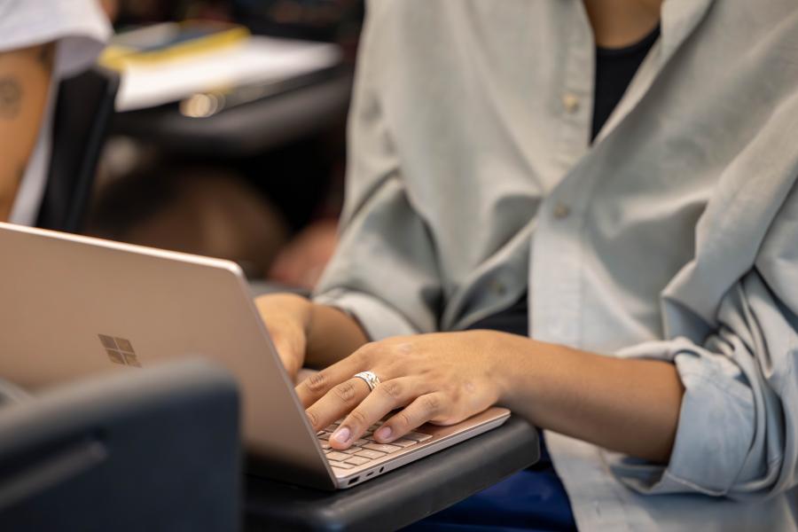 Individual typing on a laptop, only torso and hands shown.