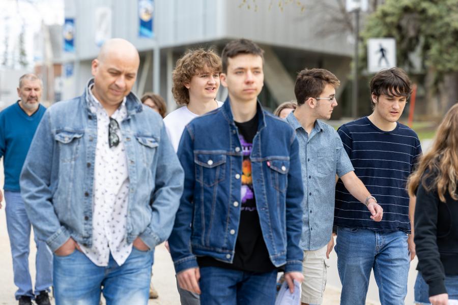 A group of 5 students crossing the a street in front of a university building. 