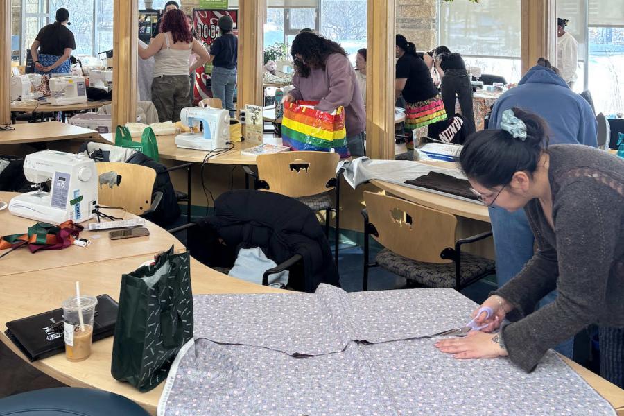 A group of several people are standing at tables putting together materials to sew ribbon clothes.