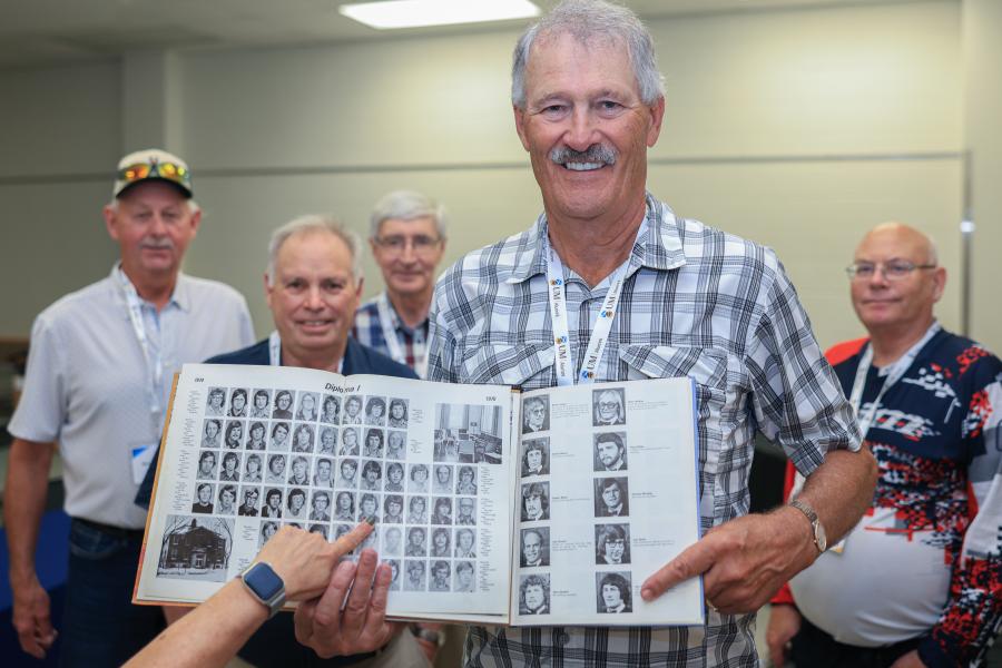 Jim Pallister pointing at yearbook photo with classmates posing in background