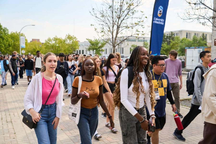 Group of students walks on campus with a UM banner behind them. 