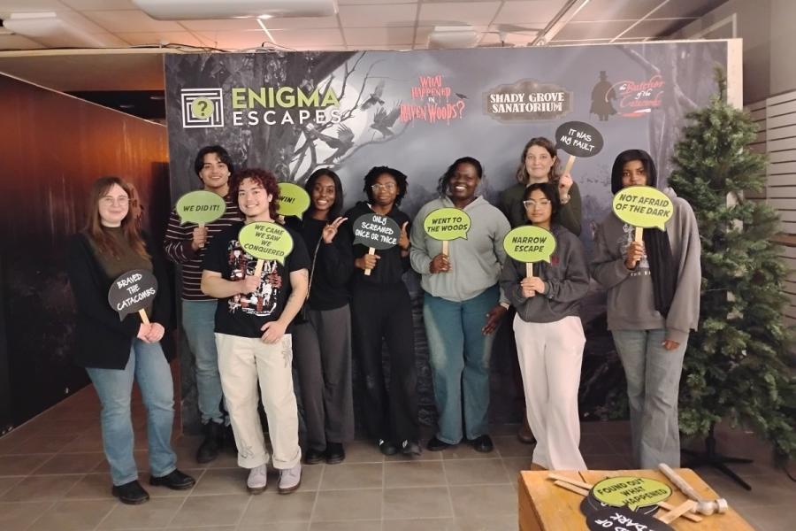 A group of people standing in front of backdrop that says 'Enigma Escapes'. 