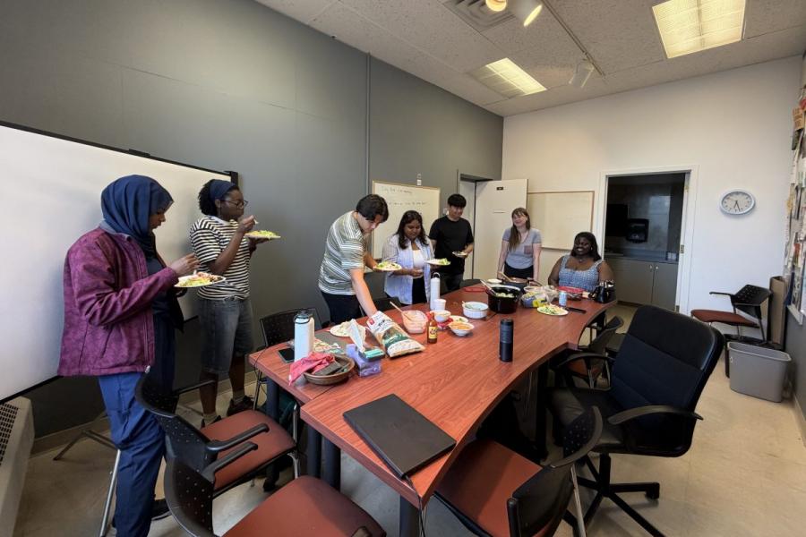 A group of people gathered around a table grabbing food to put on their plates.