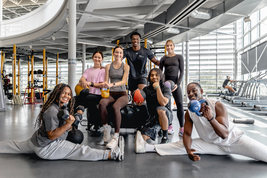 A group of seven gym-goers pose with kettlebells and weights in UM's Active Living Centre gym. 