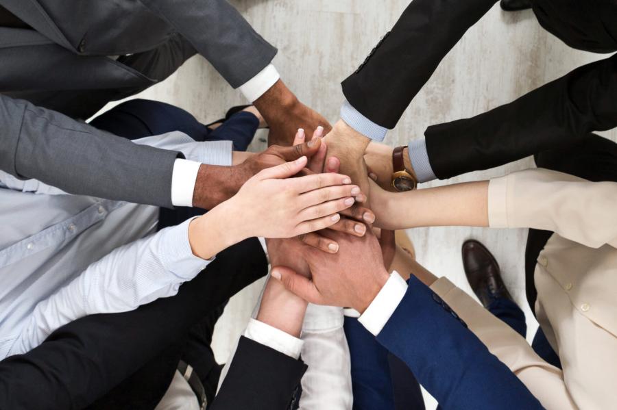 A diverse group of people stand together forming a circle and stack their hands on one another in the middle.