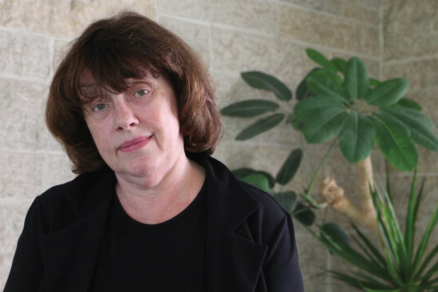 Dawne McCance in front of a beige wall and plants