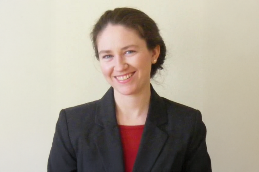 Julia Gamble in front of a beige wall with a black and red suit